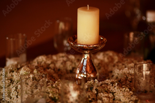 White candle stands on the sprakling holder in the middle of a w photo