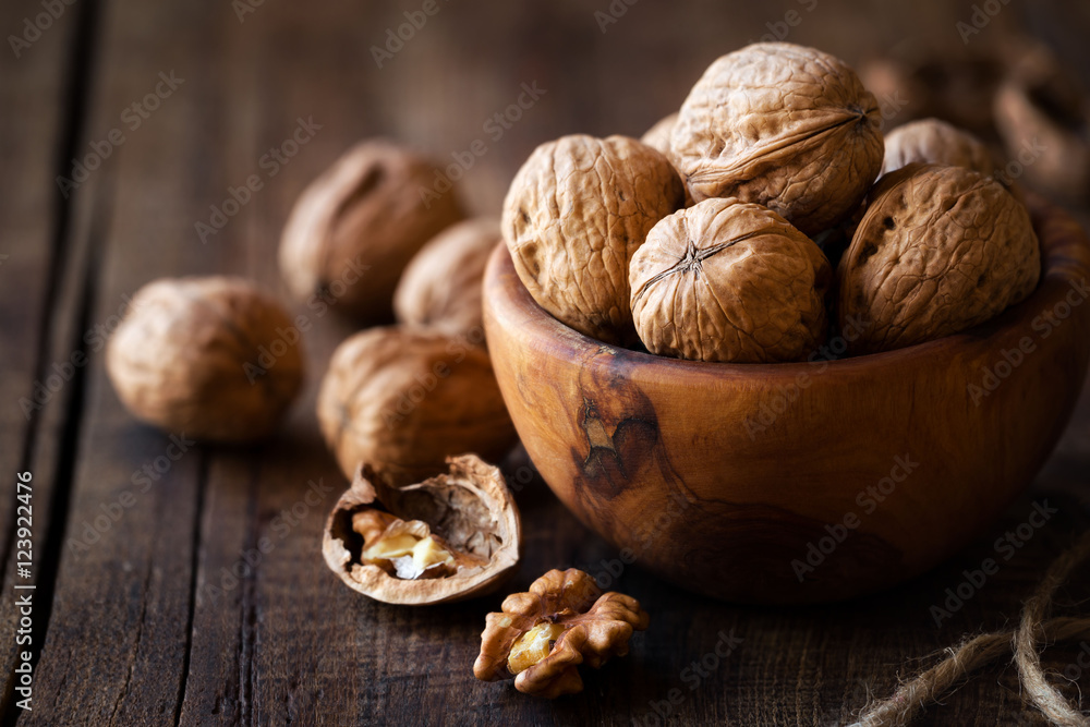 Whole walnuts and kernels in a wooden bowl against dark rustic wooden background. Shallow depth of field Whole walnuts and kernels in a wooden bowl against dark rustic wooden background. Shallow depth of field