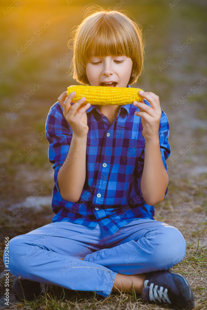Happy boy eating healthy corn on the cob - obrazy, fototapety, plakaty 
