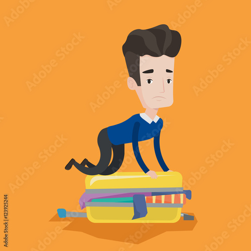 Young man trying to close suitcase.