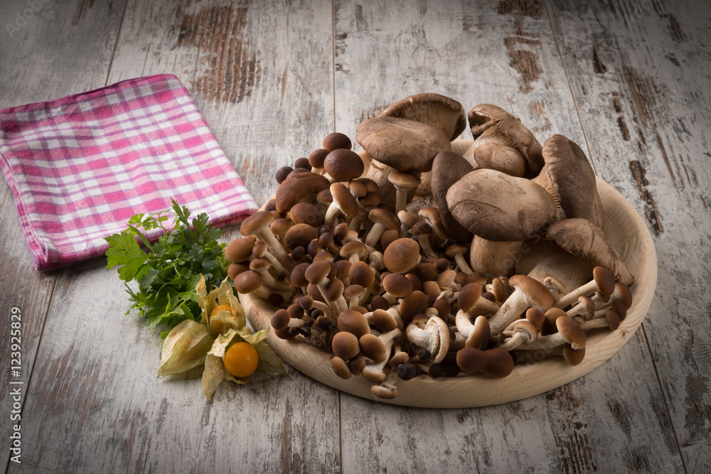 Fototapeta premium Misto di funghi freschi su un piatto tondo in legno su un tavolo 