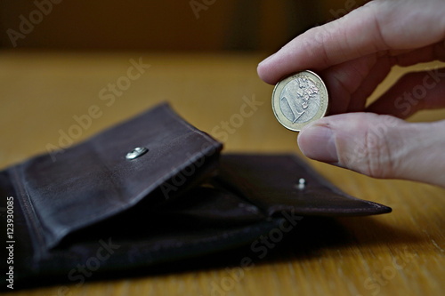 Male hand holding one Euro (European currency Euro, EUR) and withdrawing that from the brown leather wallet