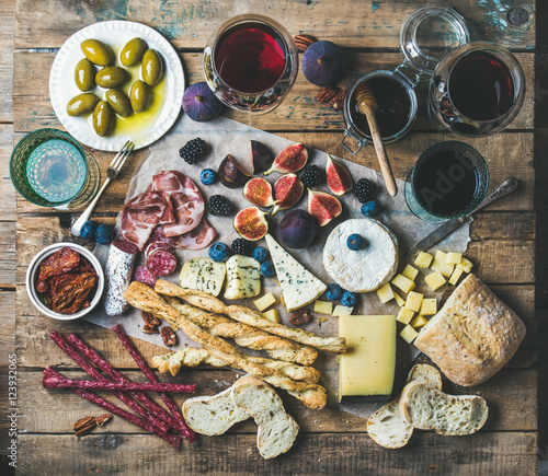 Wine and snack set with various wines in glasses, meat variety, bread, green olives, figs, nuts and berries on wax paper over rustic wooden background, top view, horizontal composition © sonyakamoz