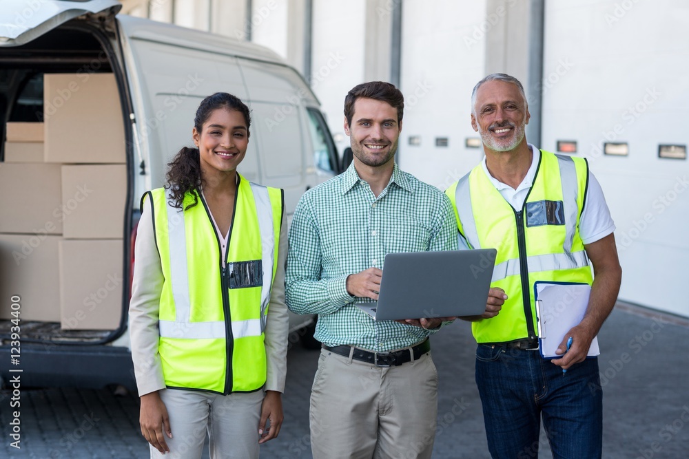 Manager and warehouse workers standing with laptop and clipboard Manager and warehouse workers standing with laptop and clipboard