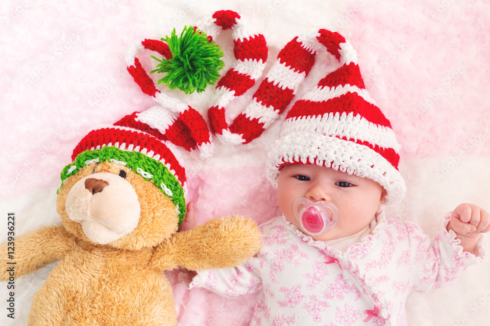 Baby girl in a Christmas hat with her teddy bear