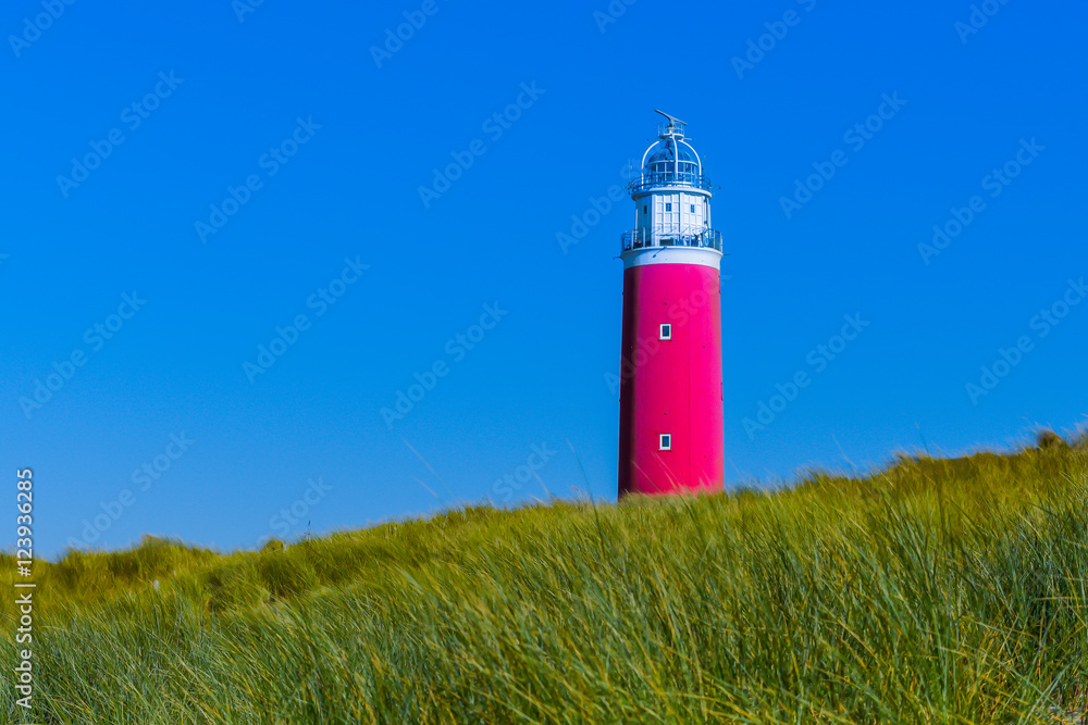 A red light house isolated in the afternoon autumn sun with beautiful blue sky background and green grass foreground