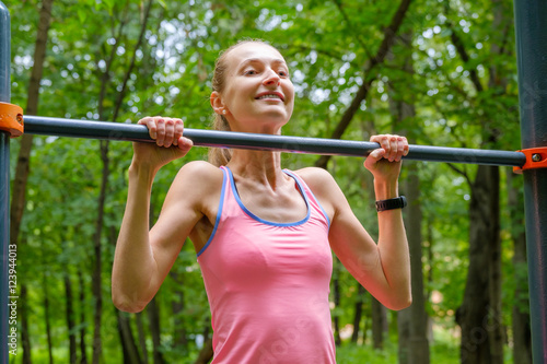 Young slim woman pulls on horizontal bar in a park