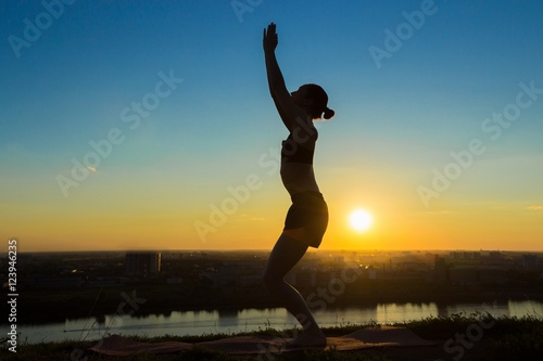 Silhouette of sporty woman practicing yoga in the park at sunset. Sunset light, sun lens flares, golden hour. Freedom, health and yoga concept