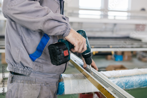 Factory for aluminum and PVC windows and doors production. Manual worker assembling PVC doors and windows and working with screw gun.