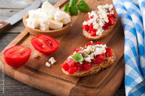 Bruschetta with tomatoes, feta cheese and basil. Traditional Greek snack on wooden background. Selective focus.