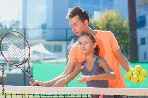 Wallpaper Mural Instructor or coach teaching child how to play tennis on a court indoor Torontodigital.ca