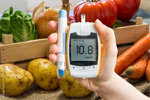 Hand holds glucometer for measuring glucose level. Vegetables in background. Isolated on white background.