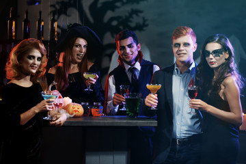 Young people in different costumes drinking cocktails at Halloween party