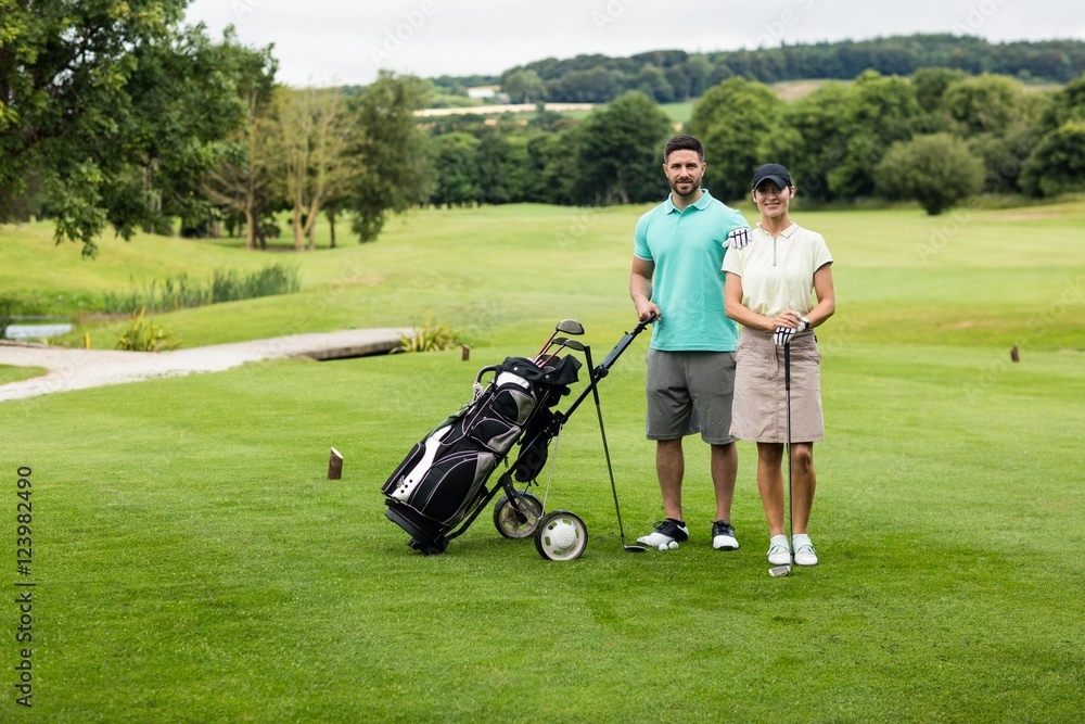 Couple standing with golf club and bag in golf course Couple standing with golf club and bag in golf course