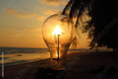 electric light bulb and sun at beach sunset sky