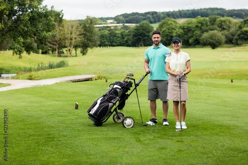 Couple standing with golf club and bag in golf course