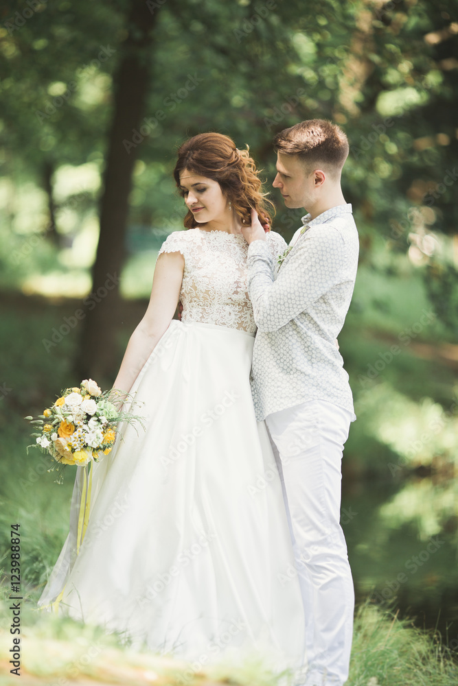 Stylish couple of happy newlyweds walking in the park on their wedding day with bouquet