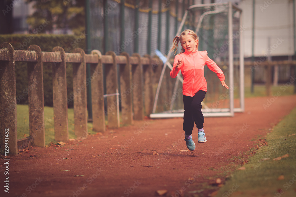 Young girl aged 5-7 running on athletic race track