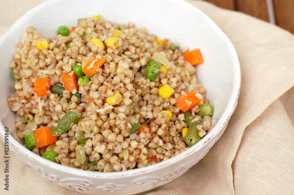Healthy Czech vegan meal, buckwheat with carrot, sweet corn, peas, green beans and onion in white bowl with fork on the brown cloth Healthy Czech vegan meal, buckwheat with carrot, sweet corn, peas, green beans and onion in white bowl with fork on the brown cloth