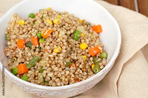 Healthy Czech vegan meal, buckwheat with carrot, sweet corn, peas, green beans and onion in white bowl with fork on the brown cloth