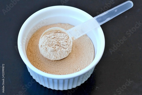 Plant protein powder from rice a pea in white bowl with plastic spoon on black background