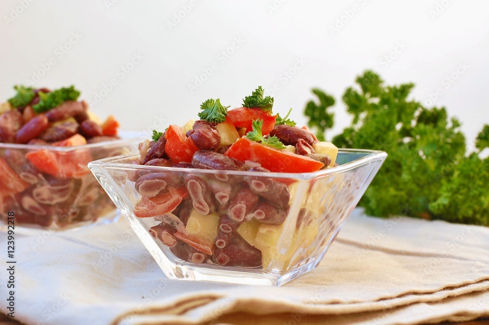 Fresh healthy vegan salad with red beans, tomato, pepper, red pepper and parsley in glass bowl on brown cloth on wooden background