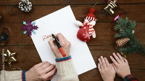 Top view of woman with red marker writing message to Santa Claus sitting at wooden table  with her little daughter. Christmas gift letter concept. 