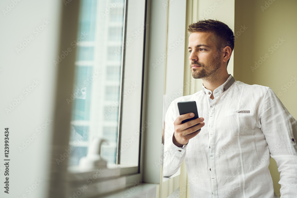 Businessman standing by the window and holding his smart phone. Businessman standing by the window and holding his smart phone.