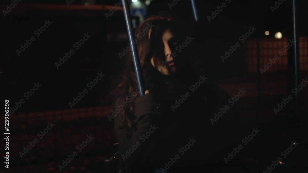 Sad lonely girl riding at night on a swing in the park Sad lonely girl riding at night on a swing in the park