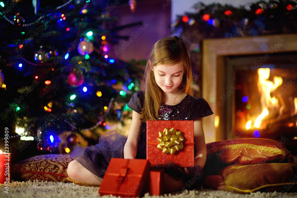 Happy girl opening Christmas gifts by a fireplace Happy girl opening Christmas gifts by a fireplace