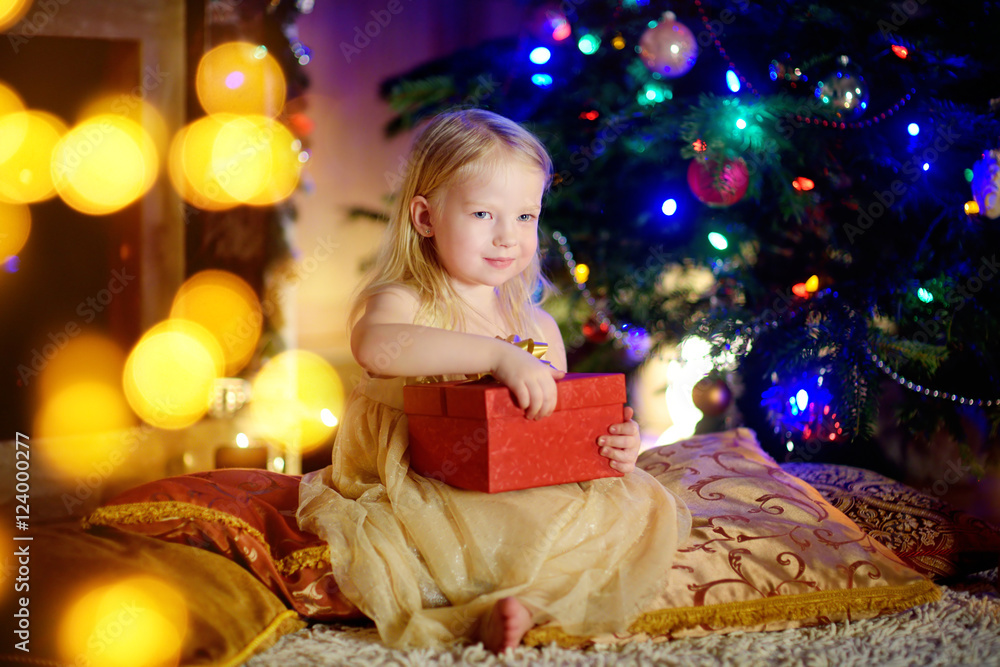 Happy girl opening Christmas gifts by a fireplace Happy girl opening Christmas gifts by a fireplace