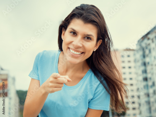 Woman in a blue shirt pointing at camera in cool cinema look