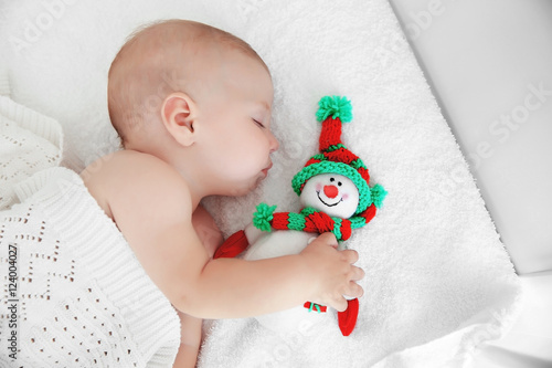 Little baby sleeping with toy snowman on white bed