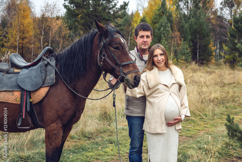 pregnant girl and her husband standing next to the horse