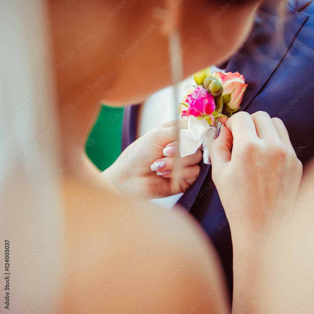A look from bride's shoulder on her hands pinning a boutonniere A look from bride's shoulder on her hands pinning a boutonniere