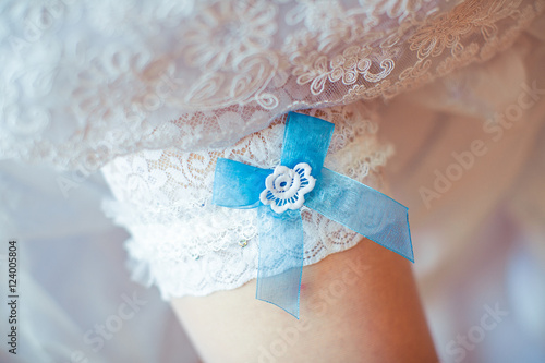 White lace garter decorated with blue ribbon put on bride's leg