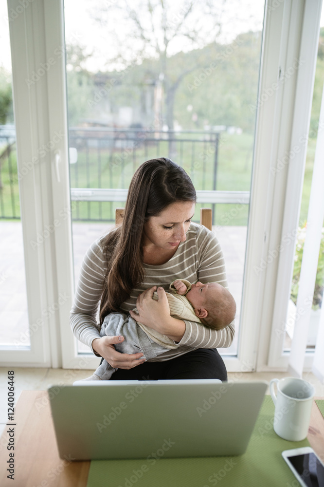Young mother holding baby son, notebook on table Young mother holding baby son, notebook on table