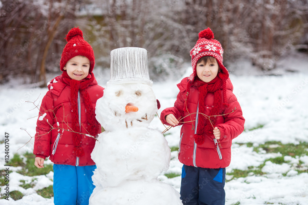 Happy beautiful children, brothers, building snowman in garden Happy beautiful children, brothers, building snowman in garden