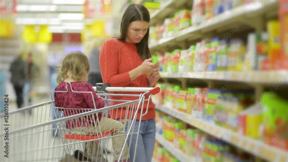 Mother and child walks along wholesale shelves and taking goods in shop trolley, beautiful young wife shopping in a supermarket Mother and child walks along wholesale shelves and taking goods in shop trolley, beautiful young wife shopping in a supermarket