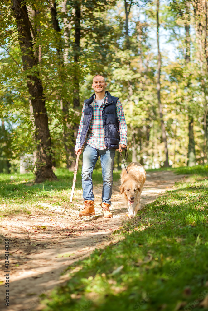Obraz premium Young man walking a dog at the park in good weather. Boy and golden retriever. Autumn environment