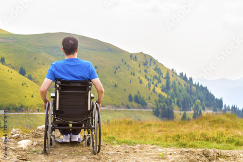 Young man in a wheelchair enjoying fresh air in a sunny day on mountain.