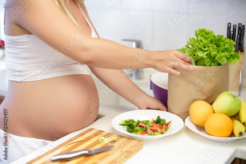 pregnant woman at kitchen preparing salad, close up