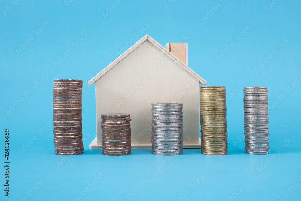 Stack of coins and wooden house symbol on blue soft background Stack of coins and wooden house symbol on blue soft background