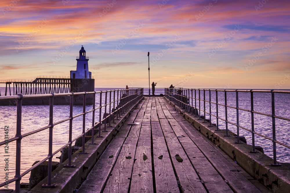 Dawn, Sunrise at Blyth Piers in Northumberland, England, UK. With anglers fishing from pier end.