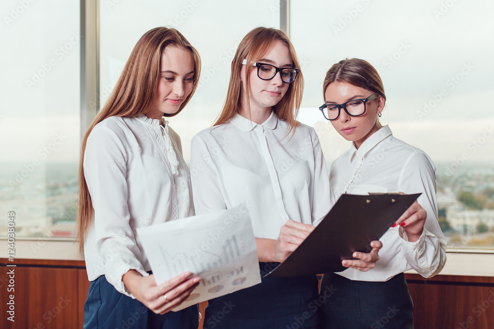 Three business women standing against the window and study the documents Three business women standing against the window and study the documents