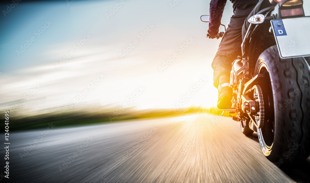 Naklejka premium Motocykl jedzie na otwartej drodze wiejskiej o zachodzie słońca