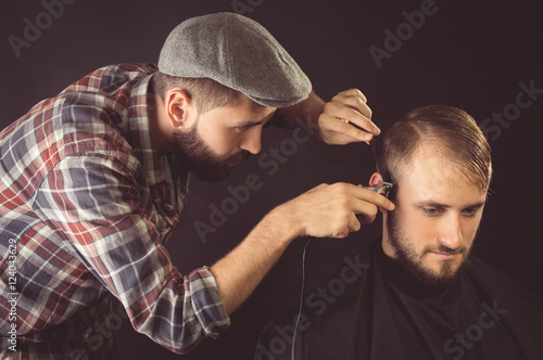 Barber shaves the hair to the client. On a black background.