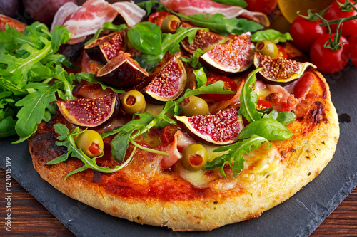 Fig pizza with bacon, green pimiento olives, rocket and basil leaves