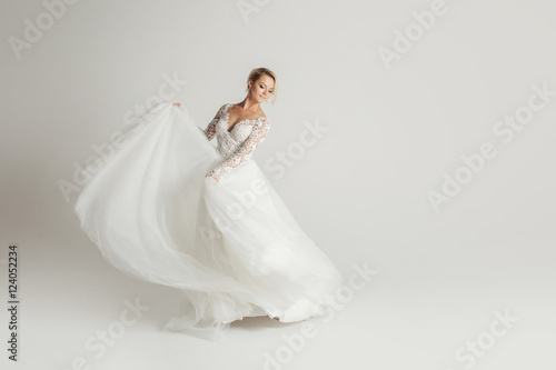 Beautiful attractive bride in wedding dress with long full skirt, white background, dance and smile