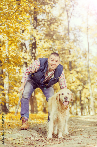 Young man walking a dog at the park in good weather. Boy and golden retriever. Autumn environment